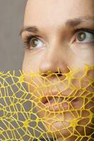 A young woman is hiding her face beneath the crochet net. Closeup photo