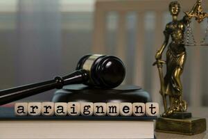 Word ARRAIGNMENT composed of wooden dices. Wooden gavel and statue of Themis in the background. photo