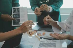 Multiracial medical team having a meeting with doctors in white lab coats and surgical scrubs seated at a table discussing a patients records photo