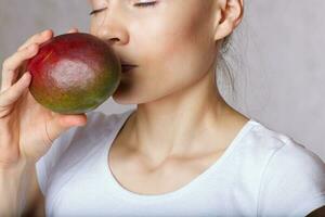 Young lady is keeping mango close to her face. Closeup photo