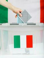 Female hand keeps ballot over ballot box. Italian flag in the background. photo