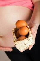 Young pregnant woman keeps woven mini basket with chicken eggs. photo
