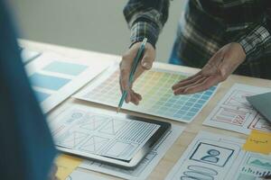 Close up ux developer and ui designer brainstorming about mobile app interface wireframe design on table with customer breif and color code at modern office.Creative digital development agency photo