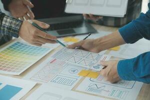 Close up ux developer and ui designer brainstorming about mobile app interface wireframe design on table with customer breif and color code at modern office.Creative digital development agency photo