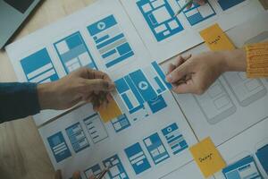 Close up ux developer and ui designer brainstorming about mobile app interface wireframe design on table with customer breif and color code at modern office.Creative digital development agency photo