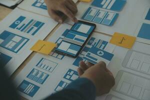 Close up ux developer and ui designer brainstorming about mobile app interface wireframe design on table with customer breif and color code at modern office.Creative digital development agency photo