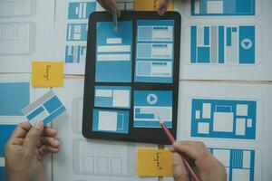 Close up ux developer and ui designer brainstorming about mobile app interface wireframe design on table with customer breif and color code at modern office.Creative digital development agency photo