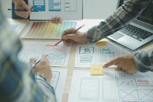 Close up ux developer and ui designer brainstorming about mobile app interface wireframe design on table with customer breif and color code at modern office.Creative digital development agency photo