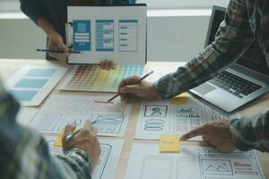 Close up ux developer and ui designer brainstorming about mobile app interface wireframe design on table with customer breif and color code at modern office.Creative digital development agency photo