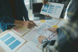 Close up ux developer and ui designer brainstorming about mobile app interface wireframe design on table with customer breif and color code at modern office.Creative digital development agency photo