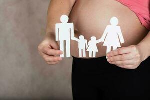 Young pregnant woman keeps paper cutouts of a family. Closeup photo
