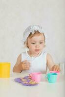 Small girl plays with toy kitchen utensils and dishes. Closeup photo