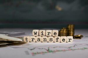 Words WIRE TRANSFER composed of wooden letter. Stacks of coins in the background. photo