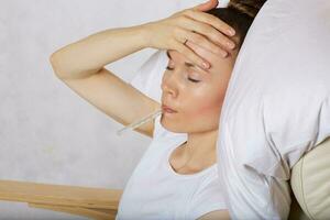 Young lady dressed in white t-shirt checks her temperature. Closeup photo