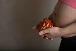 Young pregnant woman keeps natural rose blossom close to her belly. photo