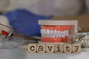 Word CAVITY composed of wooden dices. Pills, documents, pen, human jaw model in the background. photo