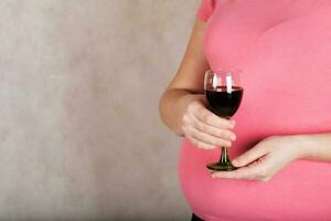 Young pregnant woman keeps a  glass of red wine. Closeup photo