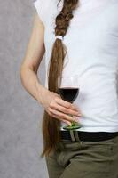 Young lady dressed in jeans keeps a glass of red wine. Closeup photo