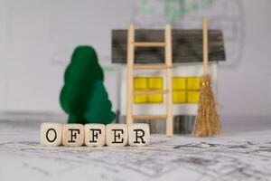 Word OFFER composed of wooden letter. Small paper house, wooden trees in the background. photo