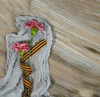 dos rosado claveles, Santo Jorge cinta en un de madera superficie. foto