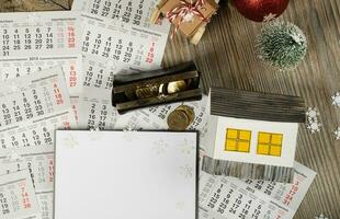 Blank sheet of paper and small paper house with coins on the New Year's background. photo