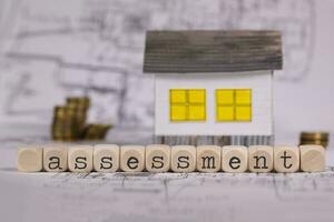 Word ASSESSMENT composed of wooden letter. Small paper house in the background. photo