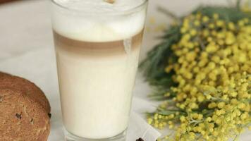 vidro do capuccino, cachos do mimosa flores, aveia biscoitos em uma de madeira superfície. video