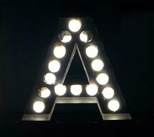 Light bulb glowing letter alphabet character A font. Front view illuminated capital symbol on black background. photo