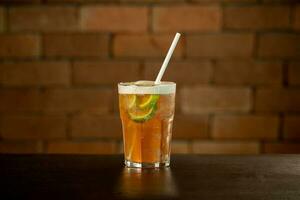 Glass of lime caipirinha drink on a table in front of a brick wall with space for text photo