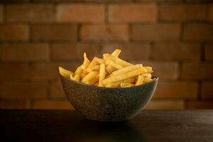 French fries in pot on table in front of brick wall photo