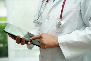 Asian woman doctor holding mobile phone or tablet for search method of treatment patient in hospital. photo