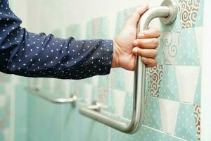 Asian woman patient use toilet support rail in bathroom, handrail safety grab bar, security in nursing hospital. photo