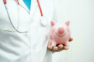 asiático mujer médico participación cerdito banco, costo de tratamiento o educación concepto. foto