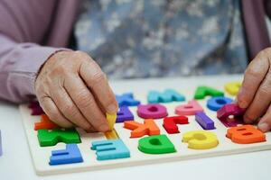 Asian elderly woman playing puzzles game to practice brain training for dementia prevention, Alzheimer disease. photo