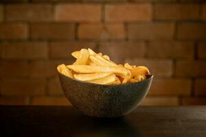 French fries in pot on table in front of brick wall photo