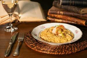 hermosa plato de camarón risotto con blanco vino. en el antecedentes antiguo libros foto