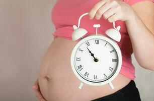 Young pregnant woman keeps vintage alarm clock close to her belly. photo