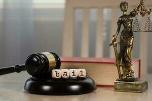 Word BAIL composed of wooden dices. Wooden gavel and statue of Themis in the background. photo