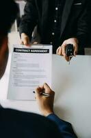 A car rental company employee is handing out the car keys to the renter after discussing the rental details and conditions together with the renter signing a car rental agreement. Concept car rental. photo