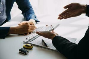 A car rental company employee is handing out the car keys to the renter after discussing the rental details and conditions together with the renter signing a car rental agreement. Concept car rental. photo