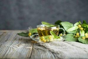 Linden blossoms tea in a glass cup on a wooden surface. photo