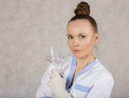 Young female gynecologist with vaginal speculum on a gray background. photo