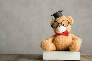 Brown teddy bear in an academic cap is placed on a thick dictionary. photo