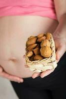 Young pregnant woman keeps woven mini basket full of nuts. photo