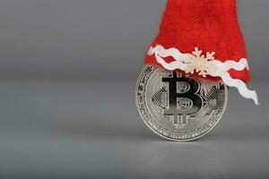 Bitcoin in a Santa Claus hat on a gray surface. photo