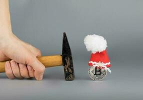 Bitcoin in a Santa Claus hat and a hammer on a gray surface. photo