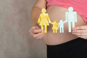 Young pregnant woman keeps paper cutouts of a family. Closeup photo