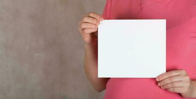 Young pregnant between 30 and 35 years old woman keeps a  blank white sheet of paper. photo