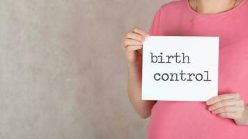 Young pregnant between 30 and 35 years old woman keeps white sheet of paper with words BIRTH CONTROL. photo
