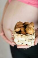 Young pregnant woman keeps woven mini basket full of nuts. photo